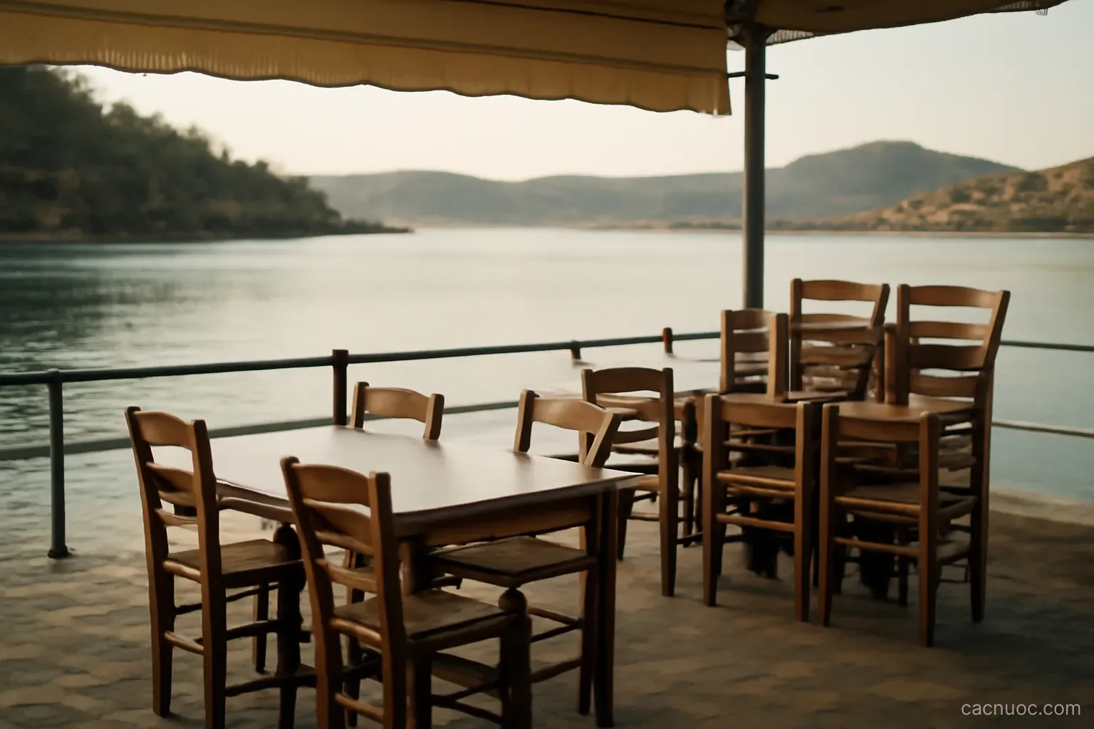 An empty seaside taverna terrace with stacked chairs facing a calm bay in low autumn light, no readable text
