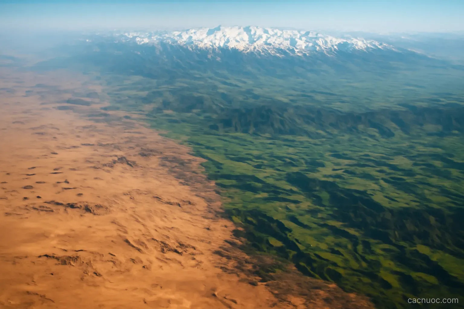 A vertical strip of contrasting terrain photographed from the air, desert fading into green valleys then snow peaks, no readable text
